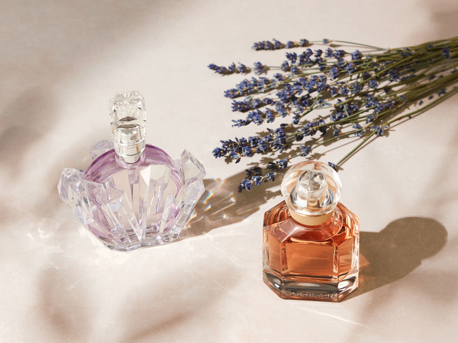 Deux flacons de parfum, l'un lilas et l'autre pêche, sont présentés à côté d'un bouquet de lavande séchée, évoquant un parfum floral et frais.