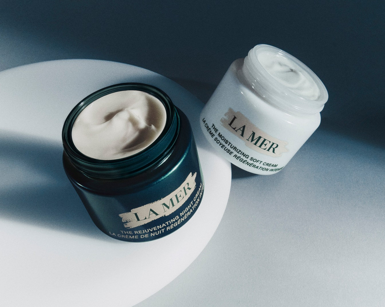 Twee potten La Mer-crème, één The Rejuvenating Night Cream in een groene pot en één The Moisturizing Soft Cream in een witte pot, beide met een zachte crème.