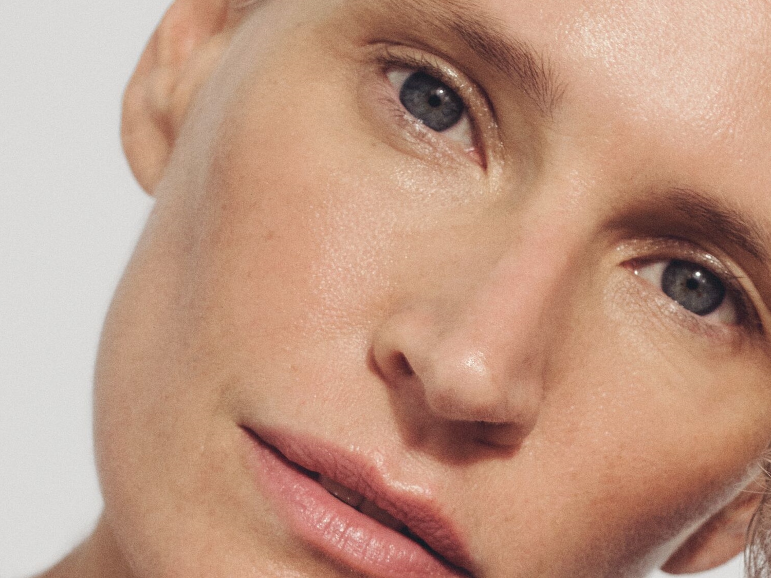 Nahaufnahme eines Frauengesichts mit strahlender Haut, hellrosa Lippen und hellblauen Augen, die einen natürlichen und frischen Look zeigen.