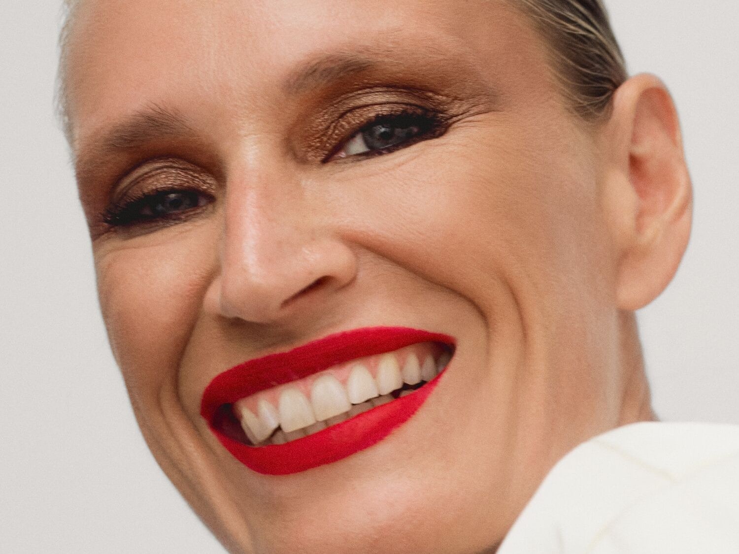 Nahaufnahme einer strahlenden Frau mit glänzendem, goldenem Lidschatten und leuchtend rotem Lippenstift, die ein gewinnendes Lächeln zeigt.