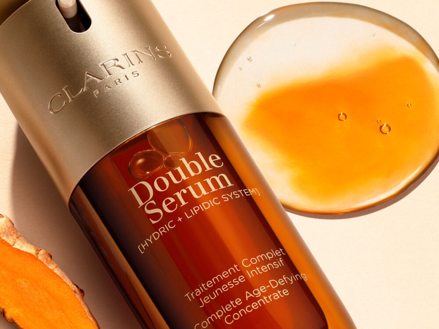 Primer plano del Double Serum de Clarins, un concentrado antiedad completo con sistema hídrico y lipídico, junto a una muestra del sérum y un trozo de cúrcuma.