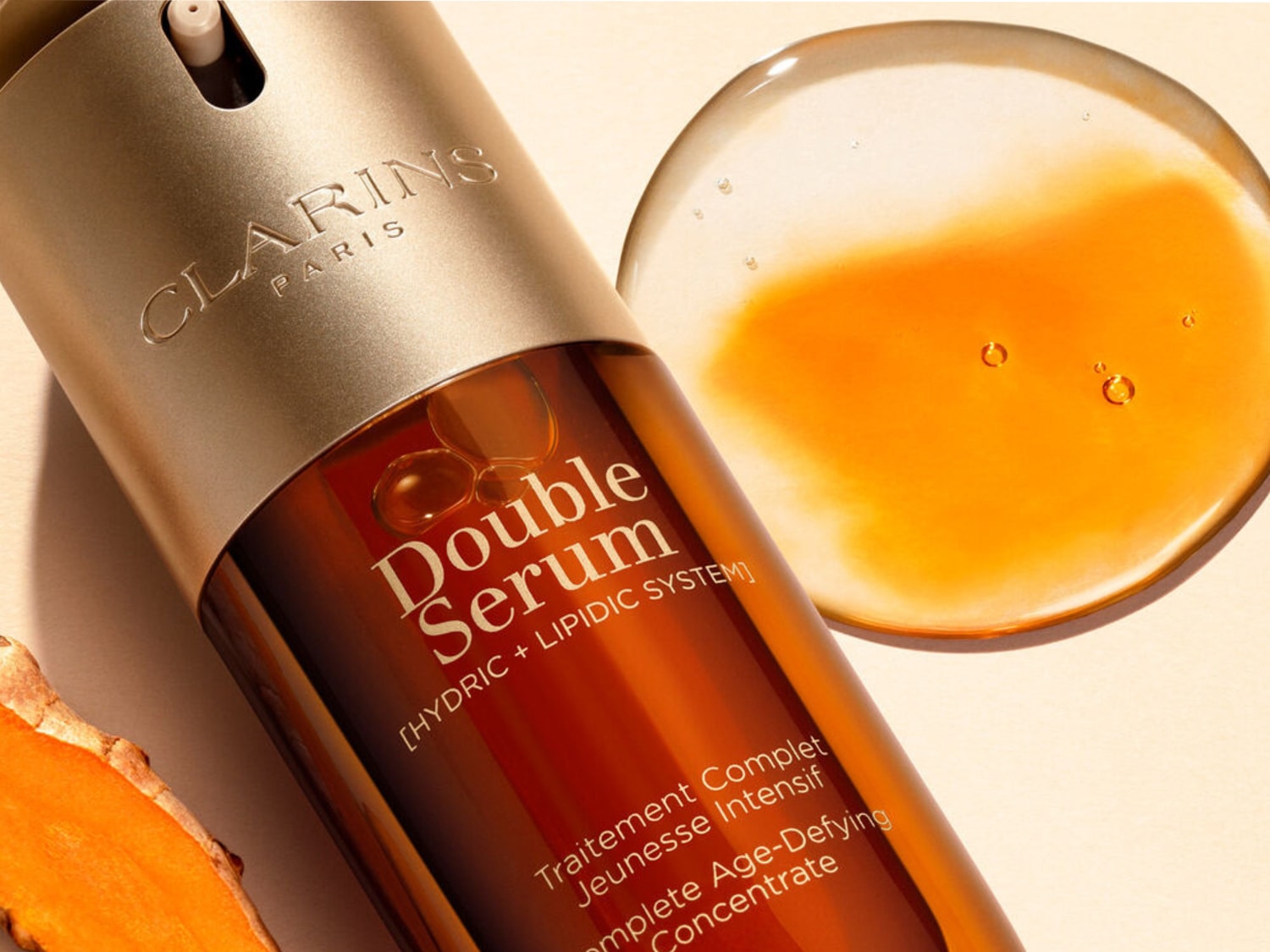 El sérum doble de Clarins, un concentrado antiedad completo con sistema hídrico y lipídico, se presenta en un envase marrón y dorado, con una gota de sérum anaranjado y brillante al lado.