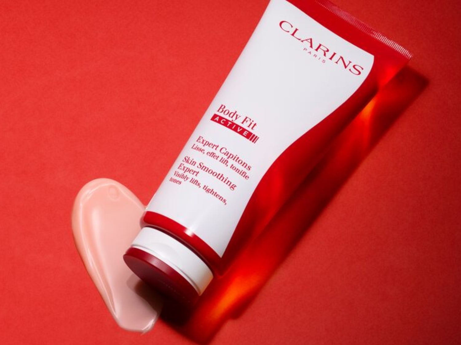 El tubo blanco de Clarins Body Fit Active, con detalles en rojo, promete alisar, levantar y tonificar la piel, junto con una muestra cremosa.
