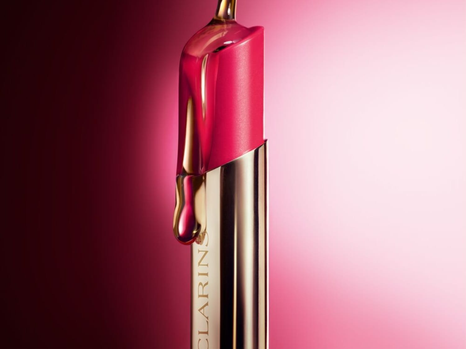 Primer plano de una barra de labios Clarins rosa brillante con aceite dorado que gotea sobre ella, resaltando su textura hidratante y su envase dorado.