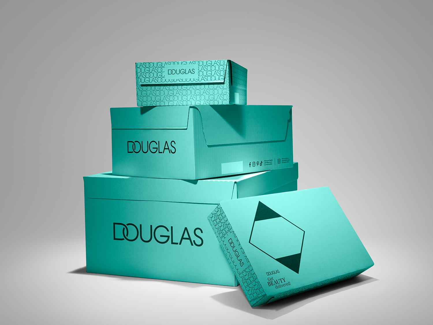 Aquí hay una pila de cajas de Douglas de color aguamarina, con el logo de Douglas en negro y el texto "Douglas Get Beauty delivered!".