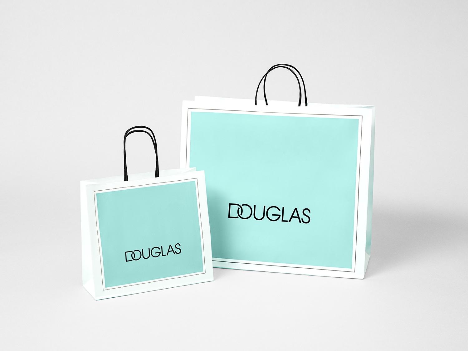 Dos bolsas de compra de Douglas, una grande y otra pequeña, ambas en color aguamarina con el logo de Douglas en negro y asas negras.