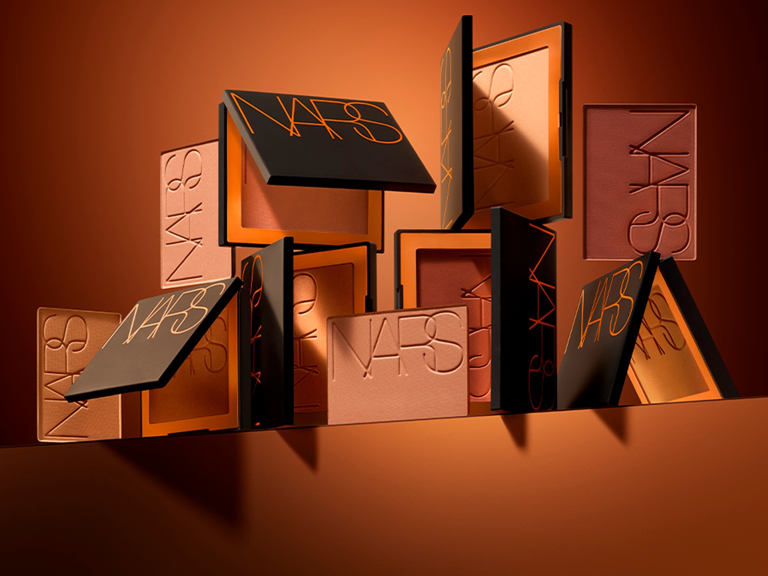Descubre la colección de coloretes NARS en tonos tierra, desde melocotón suave hasta bronce intenso, presentados en elegantes estuches negros con el logo naranja.