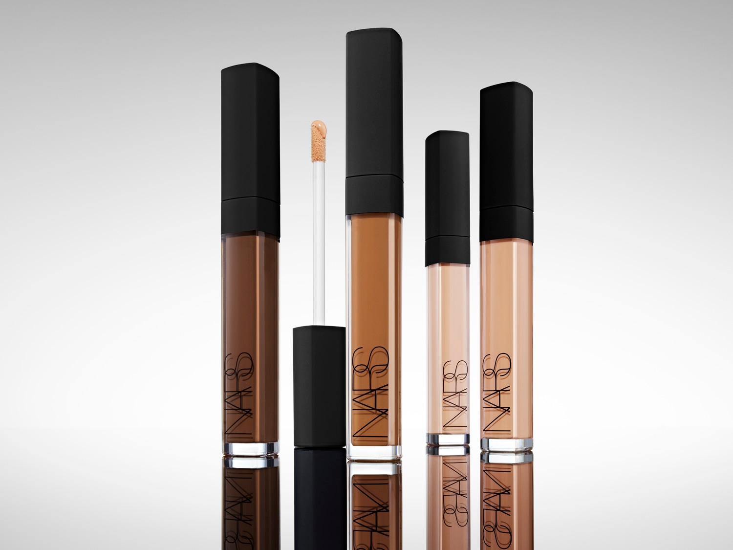 Aquí tienes correctores NARS en varios tonos, desde el marrón oscuro hasta el beige claro, cada uno con un aplicador y un elegante envase con la marca.