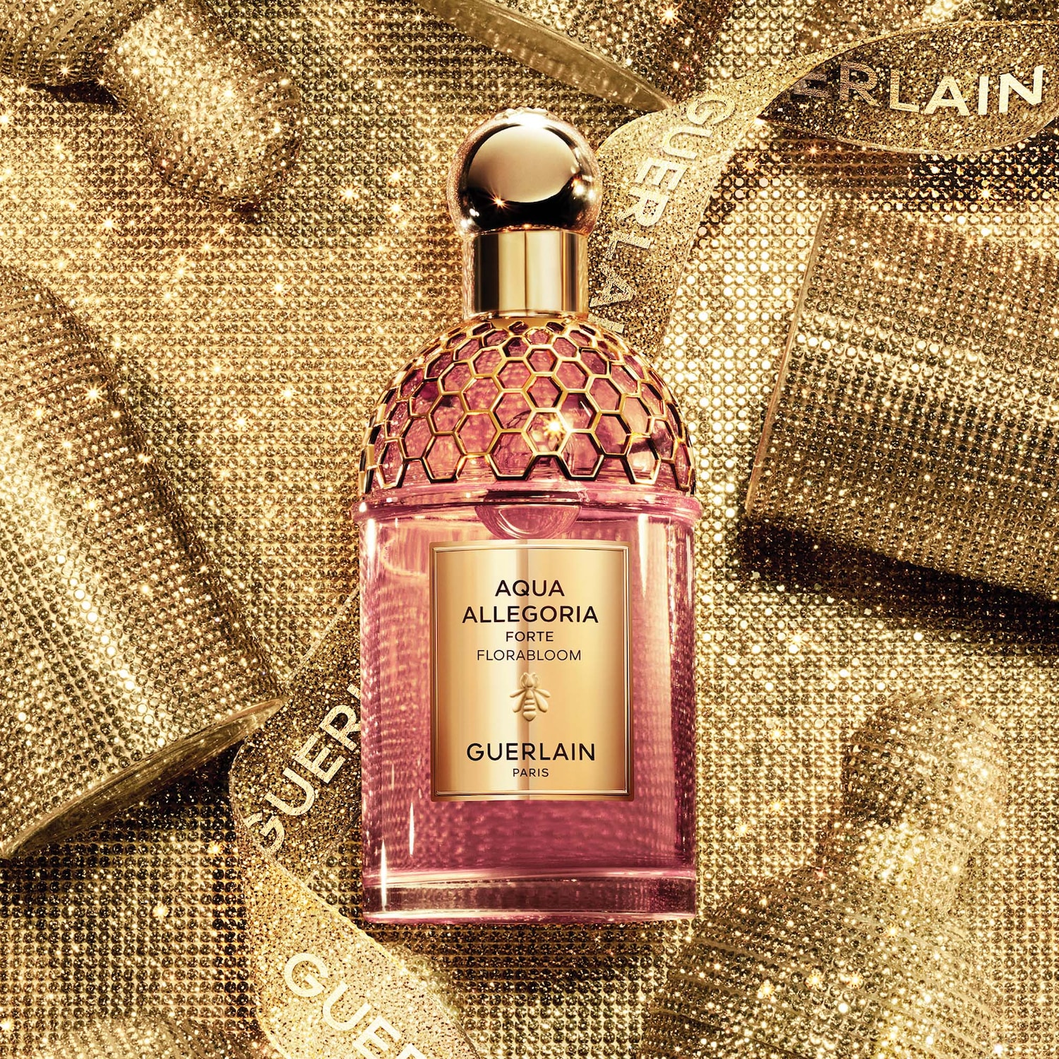 Découvrez Aqua Allegoria Forte Florabloom de Guerlain, un parfum floral rosé présenté dans un flacon orné d'un motif en nid d'abeille doré, sur un fond scintillant doré.