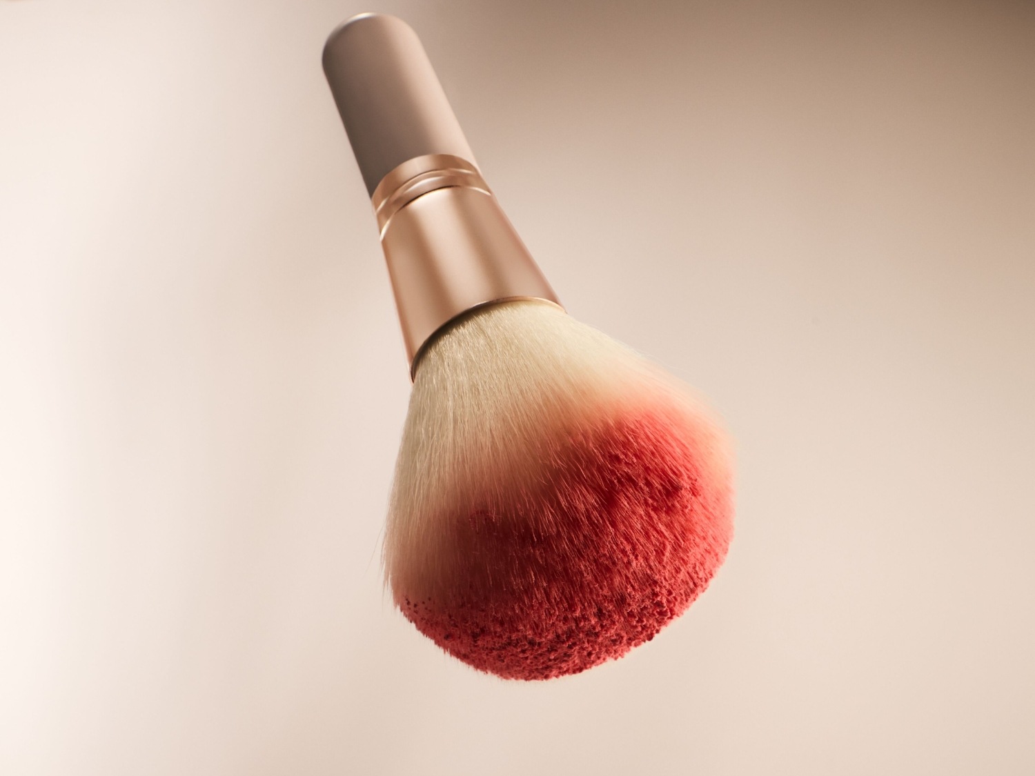 Pędzel do makijażu z miękkim, białym włosiem, którego końcówki są zabarwione na czerwono-różowy kolor, idealny do nakładania różu lub pudru.