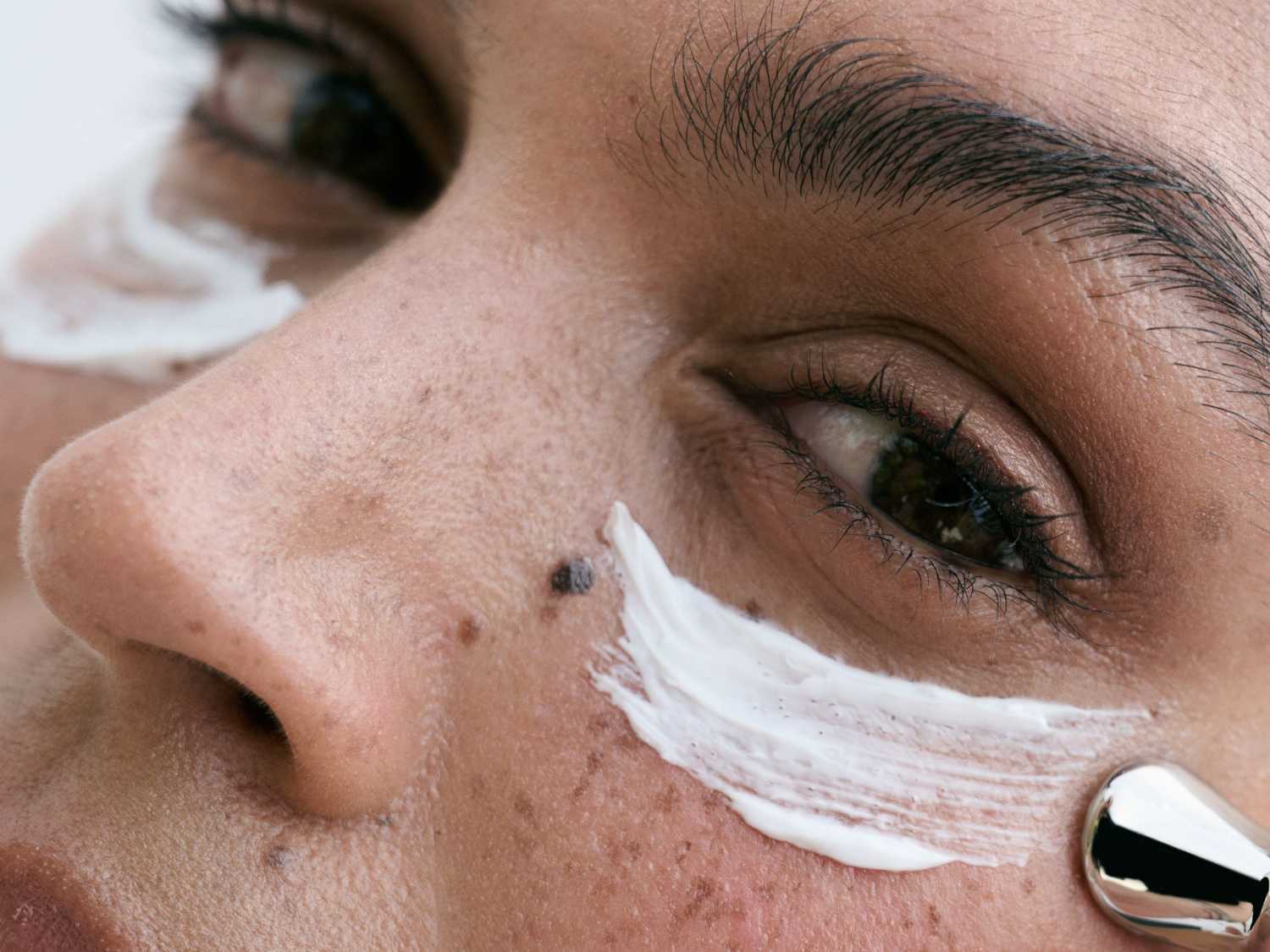 Zbliżenie na twarz z nałożonym białym kremem i metalowym aplikatorem, ukazujące pielęgnację skóry.
