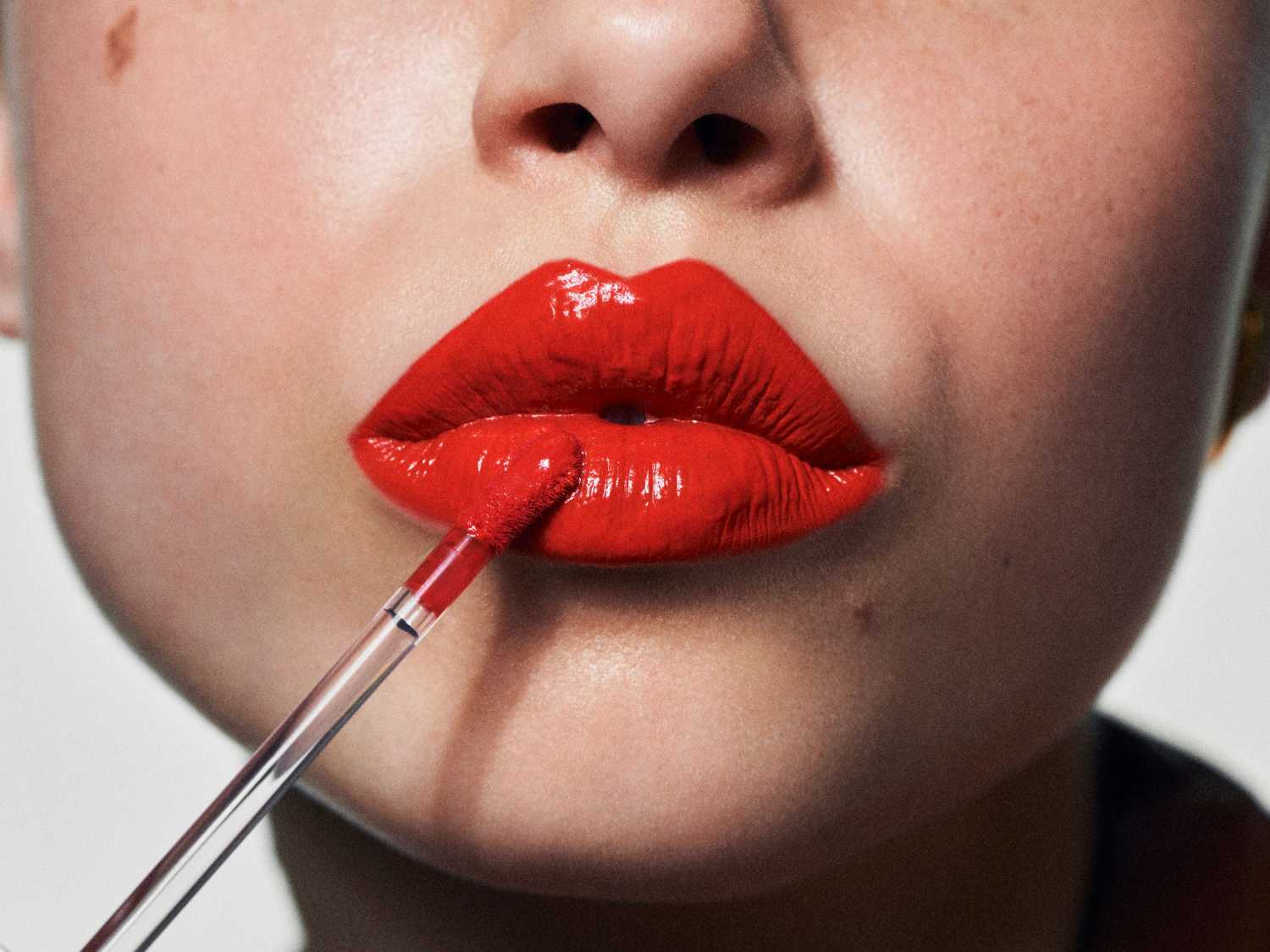 Błyszczące, czerwone usta podkreślone aplikatorem, dodające pewności siebie i blasku.