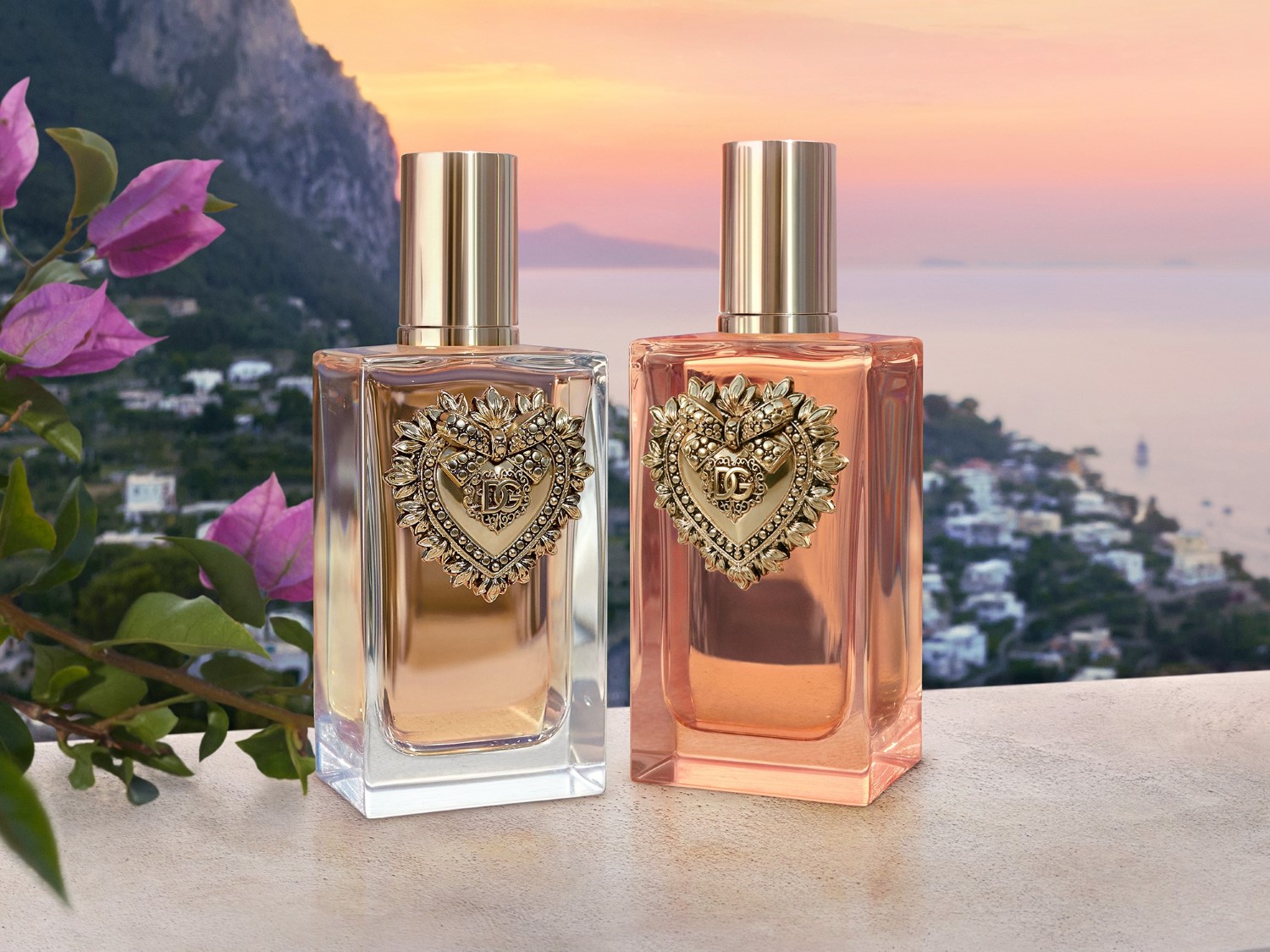 Két Dolce & Gabbana Q illat látható, egy barackos és egy borostyánszínű, mindkettőn arany szív alakú embléma van, a háttérben pedig egy festői tengerparti táj.