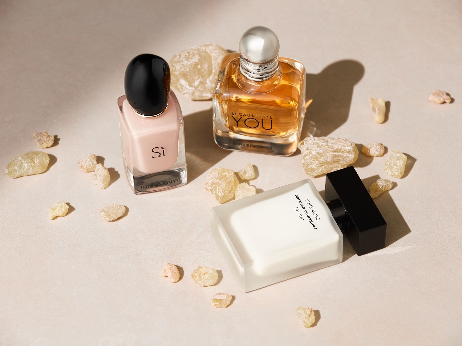 Tri parfémy sú usporiadané na stole, vrátane Giorgio Armani Si s ružovým nádychom a čiernym vrchnákom, Emporio Armani Because It's You so zlatistým odtieňom a Narciso Rodriguez Pure Musc v bielej farbe s čiernym vrchnákom.