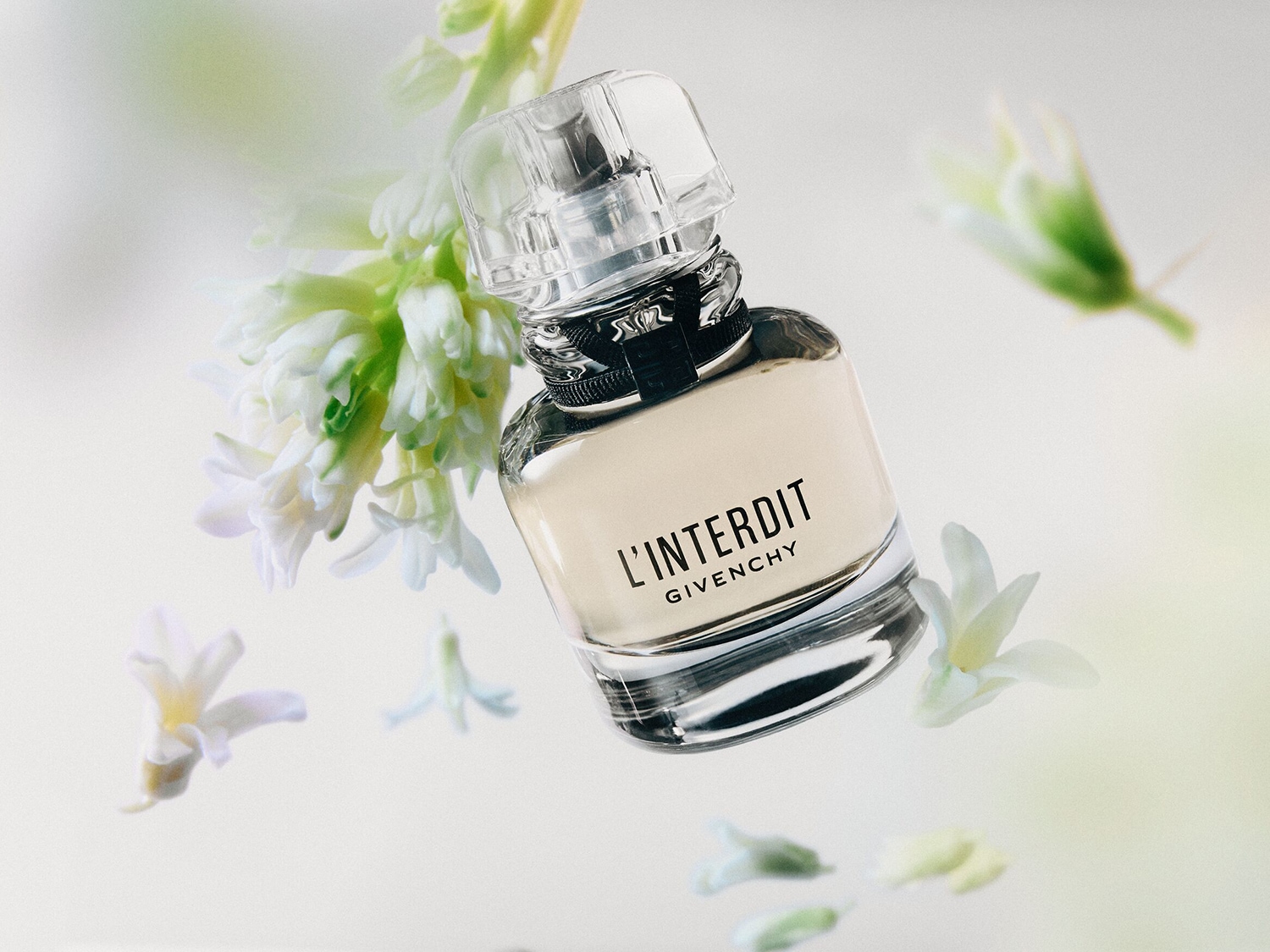 El frasco de perfume L'Interdit de Givenchy, con su diseño elegante y minimalista, se presenta con flores blancas, evocando una sensación de sofisticación y frescura.