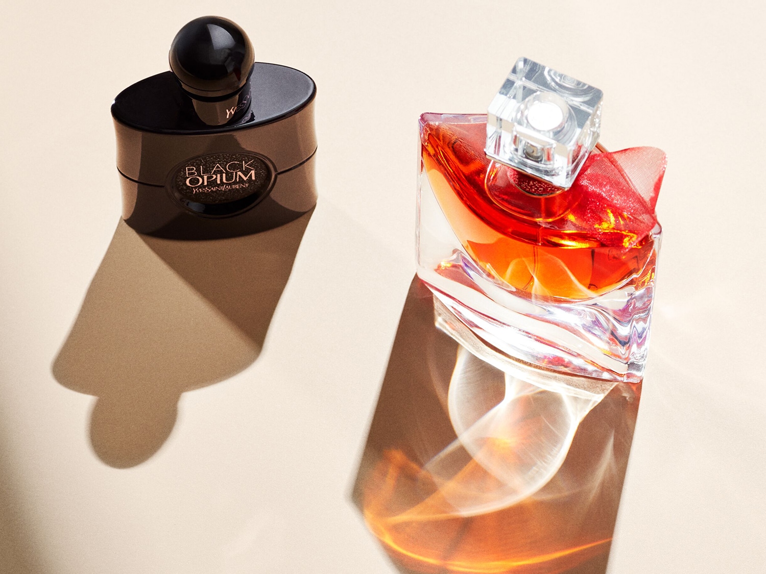 En la imagen se muestran dos frascos de perfume: uno es de color negro y lleva la etiqueta 'Black Opium' de Yves Saint Laurent, mientras que el otro es de cristal transparente con un líquido anaranjado en su interior.