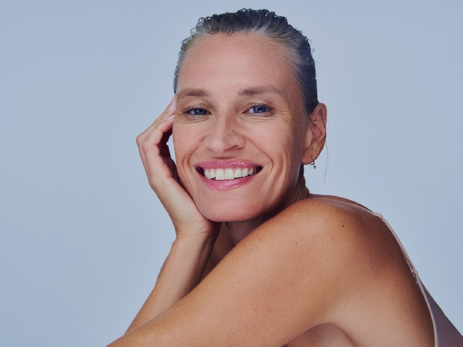 Portrait d'une femme souriante, la main sur le visage, avec une peau radieuse et un sourire éclatant.