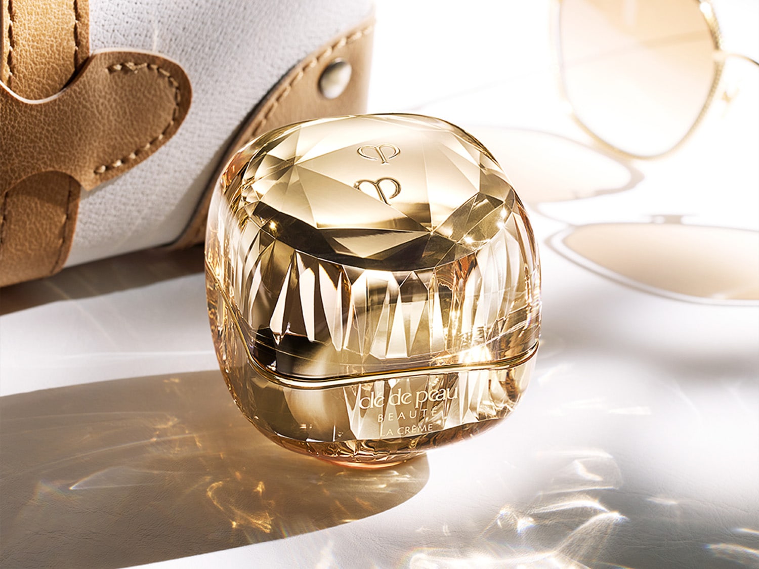 El frasco dorado facetado de Clé de Peau Beauté La Crème, con su diseño lujoso, promete una experiencia de cuidado de la piel rejuvenecedora.