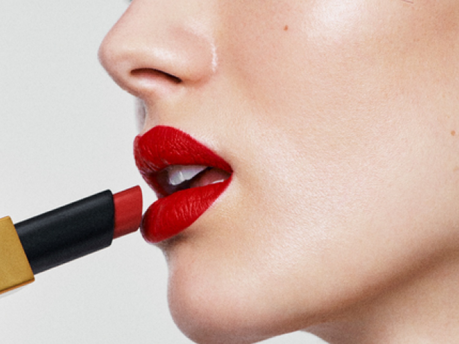 Profil kobiety aplikującej czerwoną szminkę z czarno-złotym opakowaniem, ukazujący intensywny kolor i precyzję nakładania.