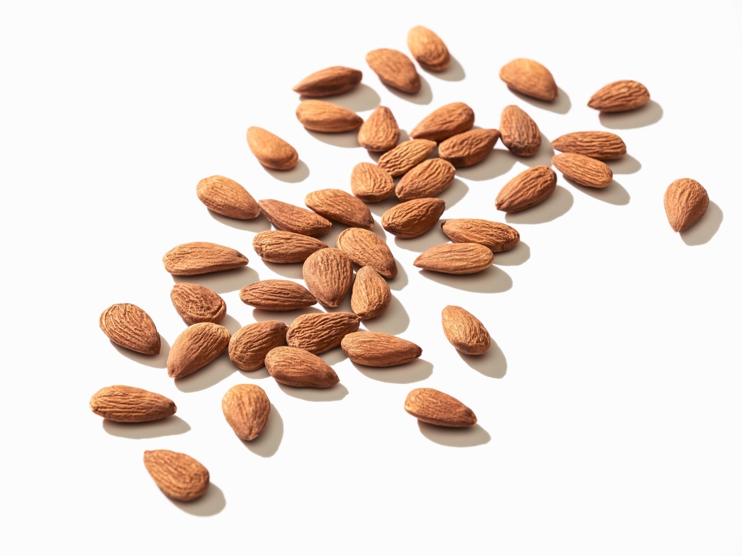 Na bielom pozadí je roztrúsená hŕstka mandlí s hnedou šupkou, pripravených na konzumáciu ako zdravý snack.
