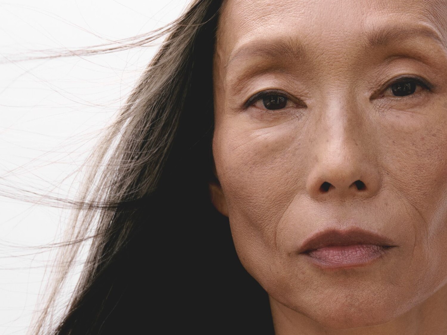 Nahaufnahme des Gesichts einer Frau mit dunklen Augen, glattem, dunklem Haar und einem natürlichen, ebenmäßigen Hautton.