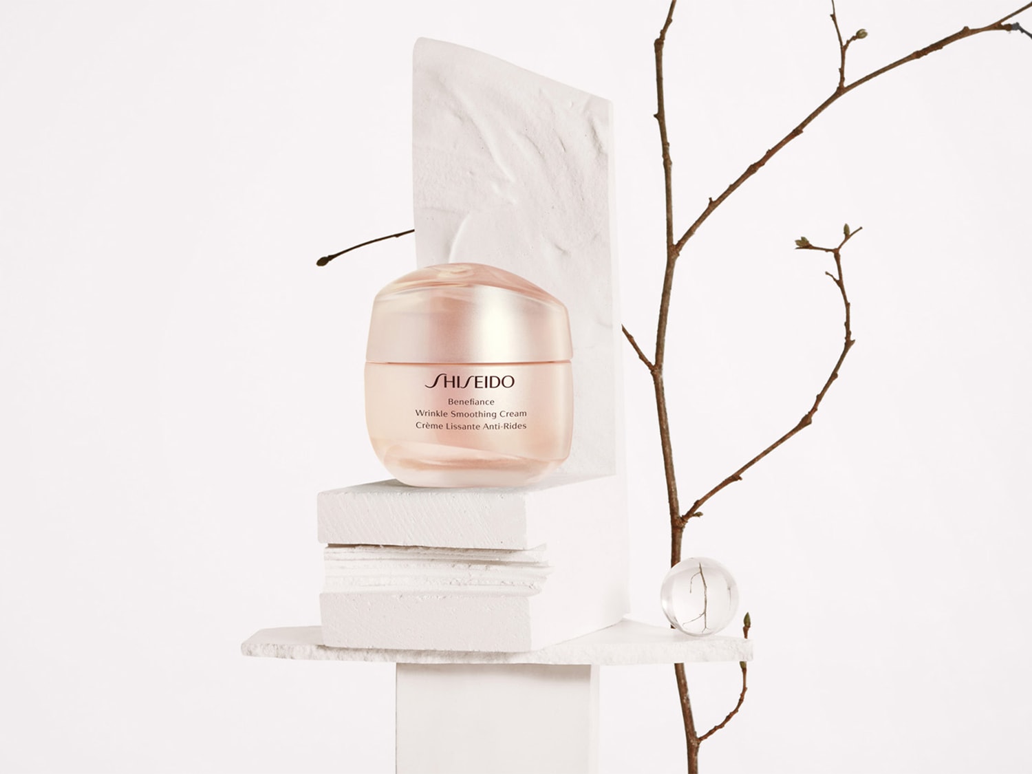 Die Shiseido Benefiance Wrinkle Smoothing Cream in einem zarten Pfirsich-Tiegel, umgeben von minimalistischen weißen Formen und einem zarten Zweig.