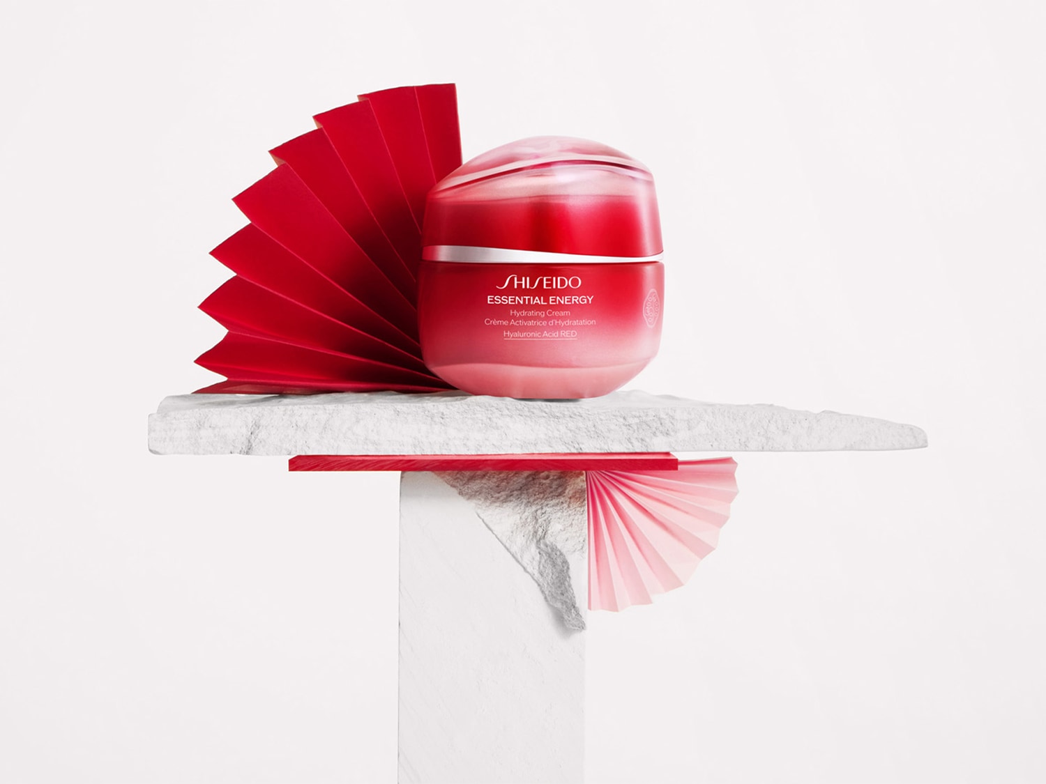 Shiseido Essential Energy Feuchtigkeitscreme in einem roten Tiegel, präsentiert mit roten Fächern auf einem weißen Sockel.