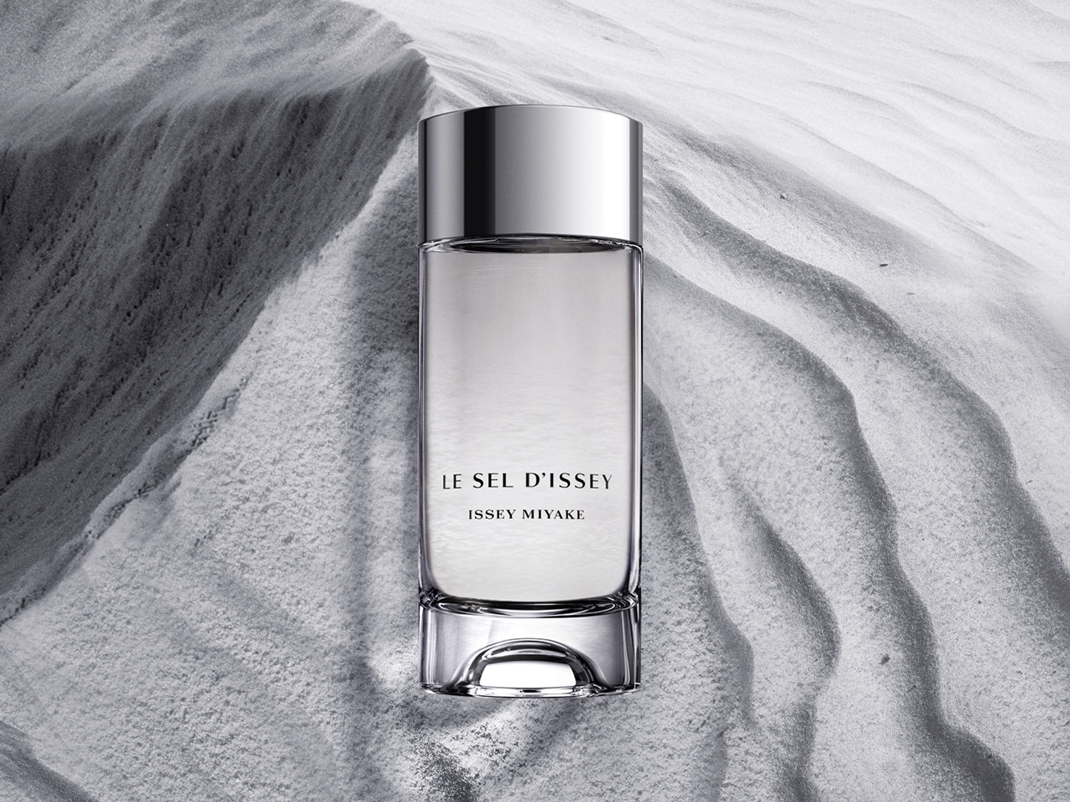 Butelka perfum Le Sel d'Issey Issey Miyake o pojemności 100 ml, z srebrną nakrętką, stoi na tle szarego piasku.