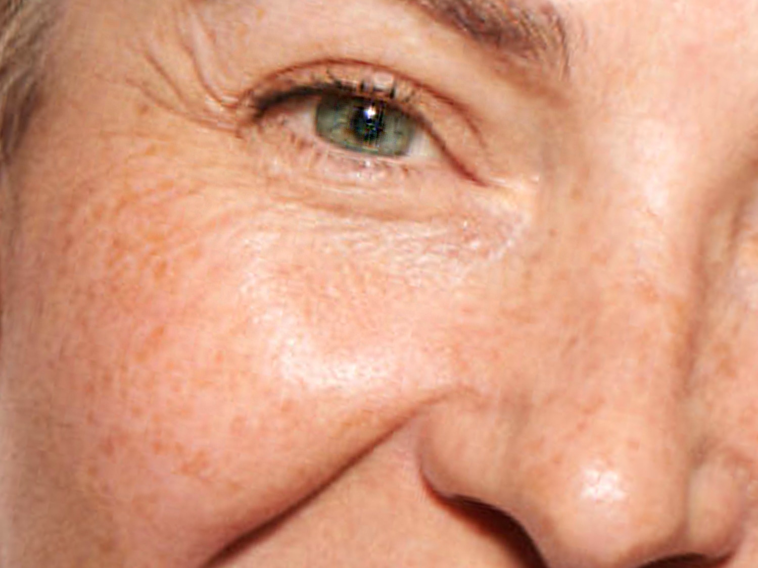 Egy nő arcának közeli képe, a zöld szemére, a ráncaira és a szeplőire fókuszálva.