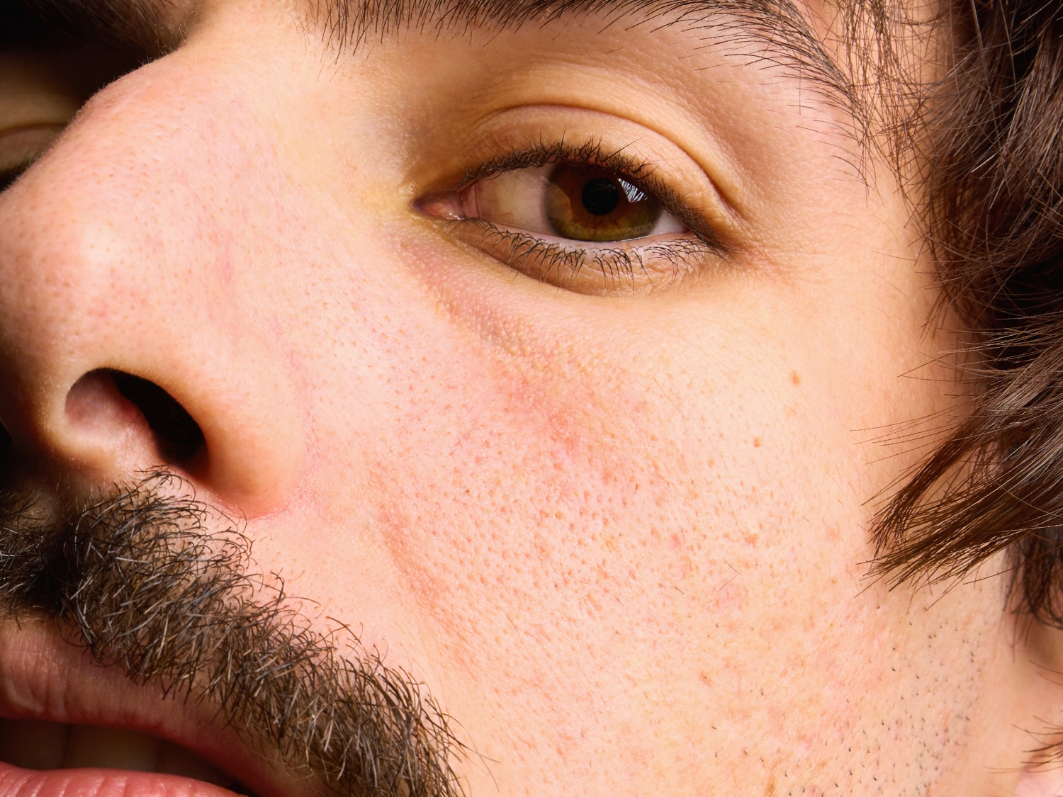 Közeli kép egy férfi arcáról, hangsúlyozva a bőr textúráját, a szakáll részleteit és a barna szemet.