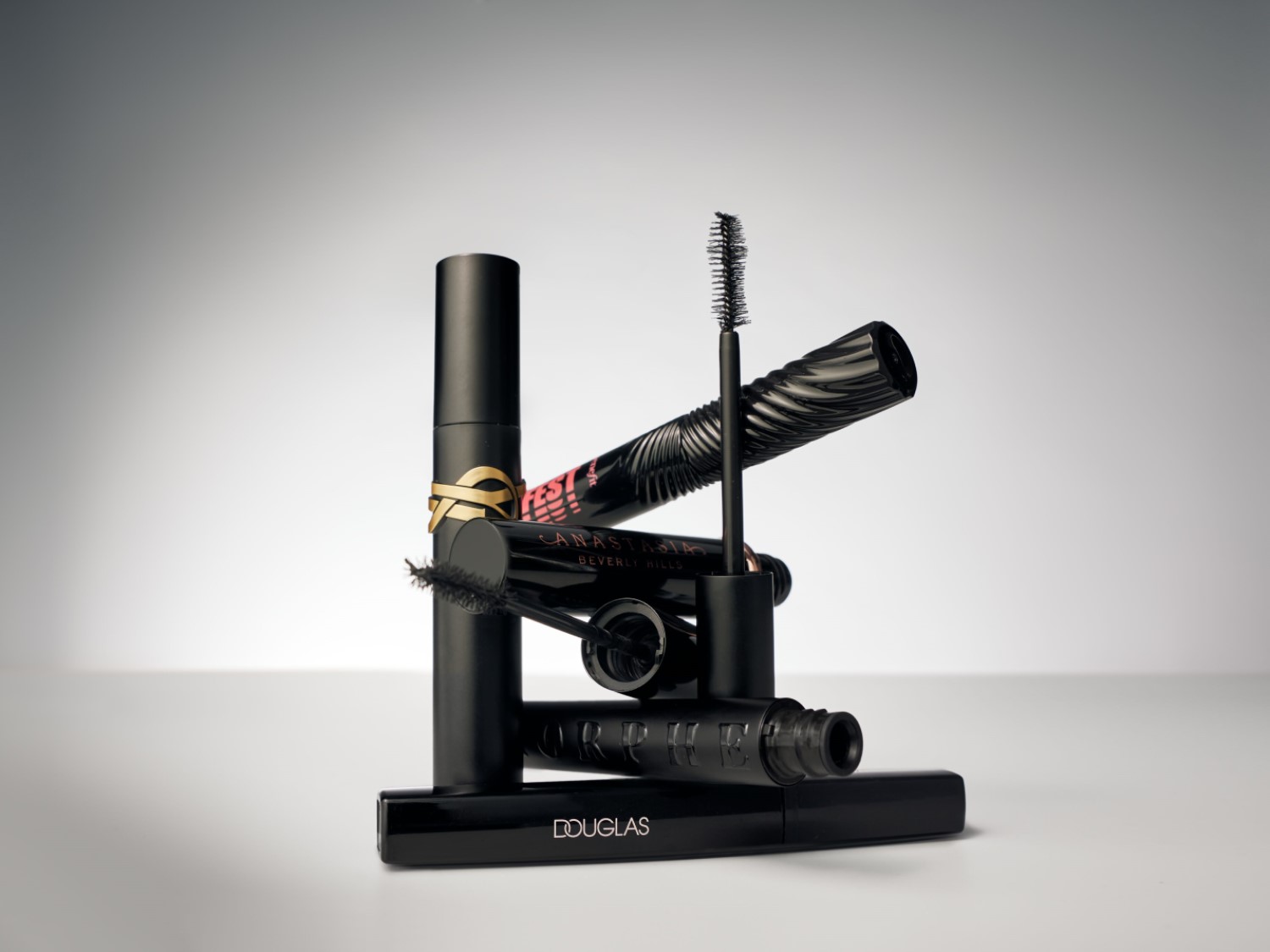 Een stapel zwarte mascara's van verschillende merken zoals Yves Saint Laurent, Anastasia Beverly Hills en Douglas.