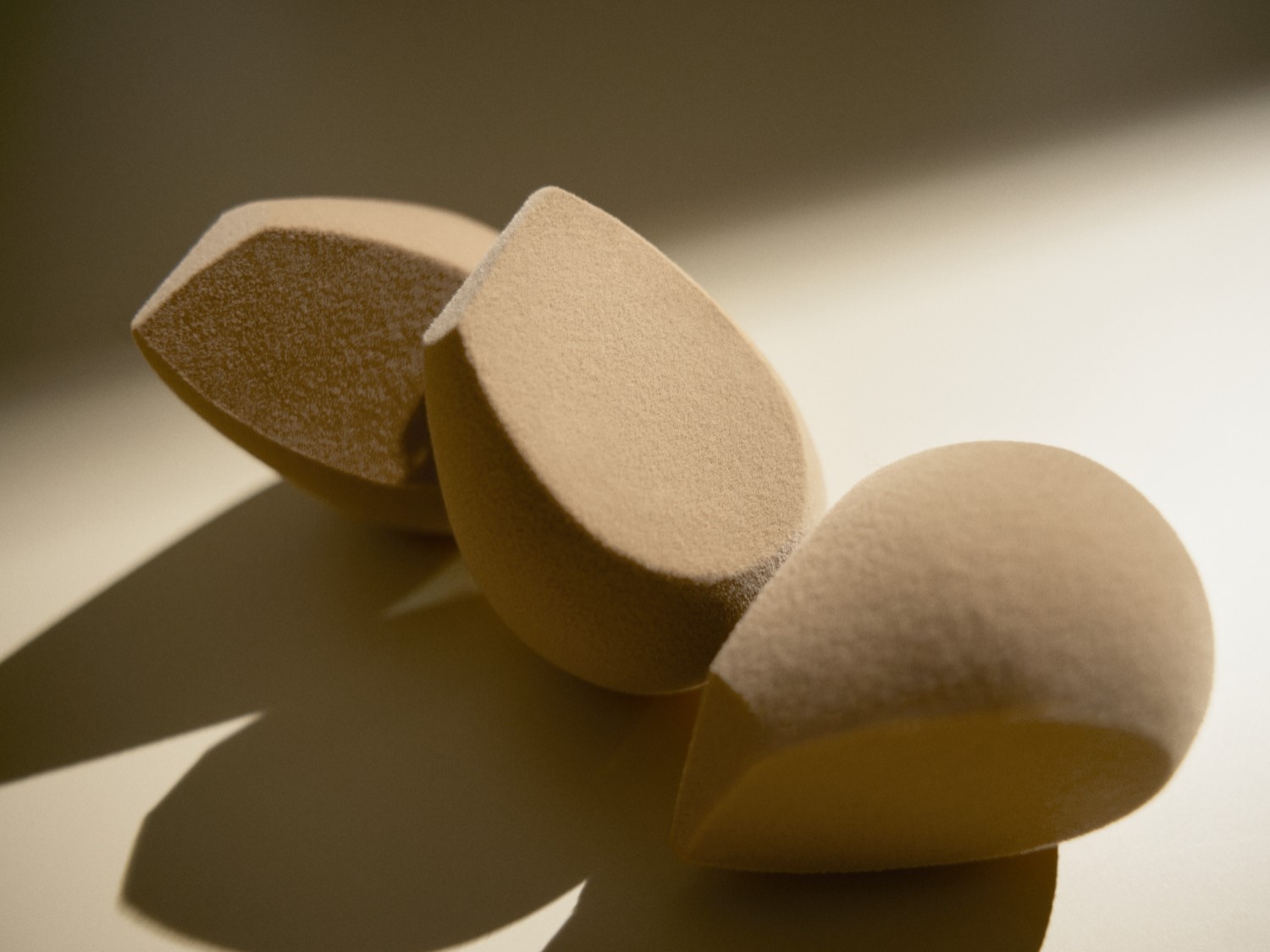 Drie beige make-upsponsjes in een druppelvorm liggen op een rij, klaar om je make-up routine te perfectioneren.
