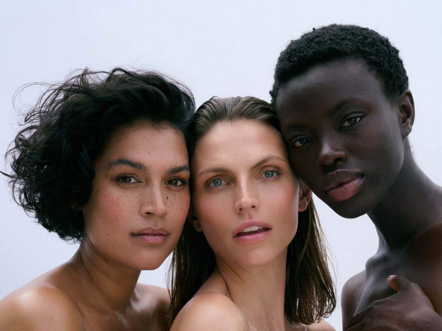 Nahaufnahme von drei Frauen unterschiedlicher Hautfarbe, die mit natürlich wirkendem Make-up und neutralen Lippen posieren.