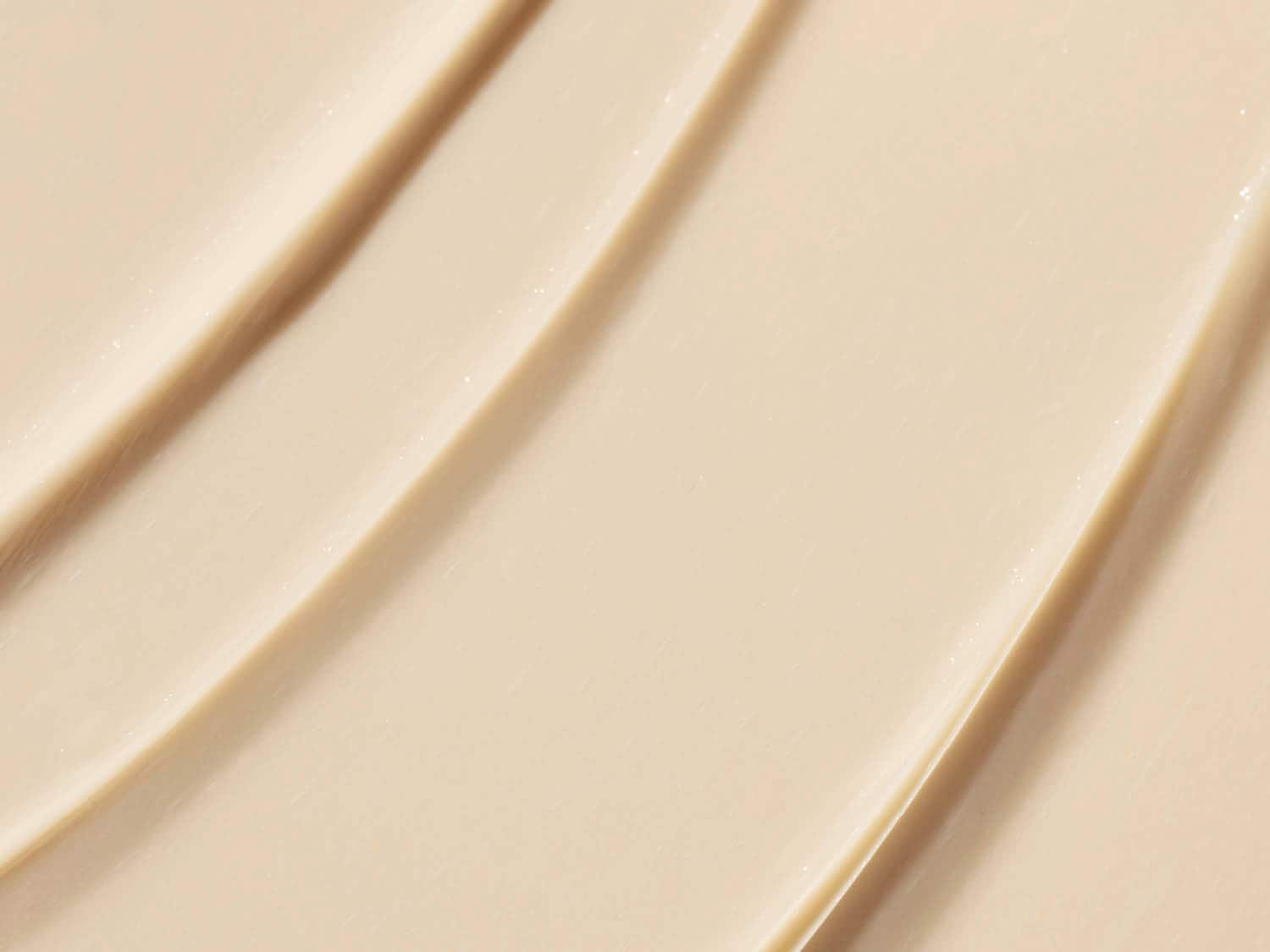De close-up toont een gladde, beige crème met subtiele glans, perfect voor het hydrateren en verzachten van de huid.