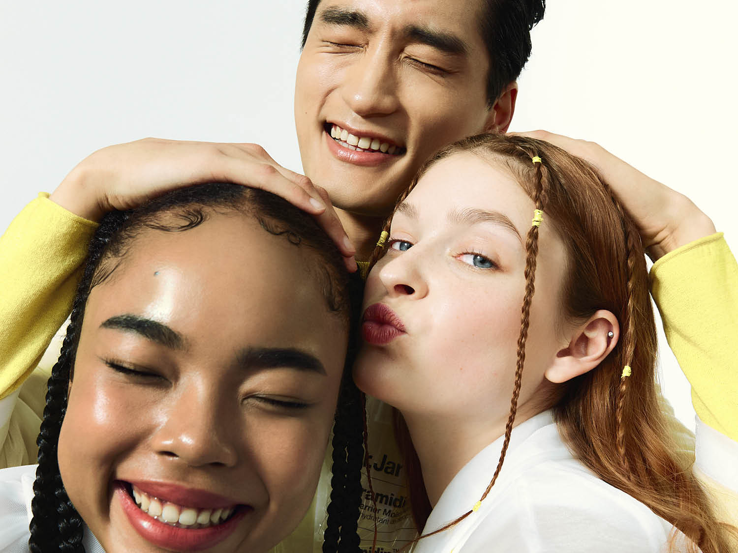 Een vrolijke foto van drie jonge mensen die knuffelen en lachen, met gevlochten haar en een stralende glimlach.