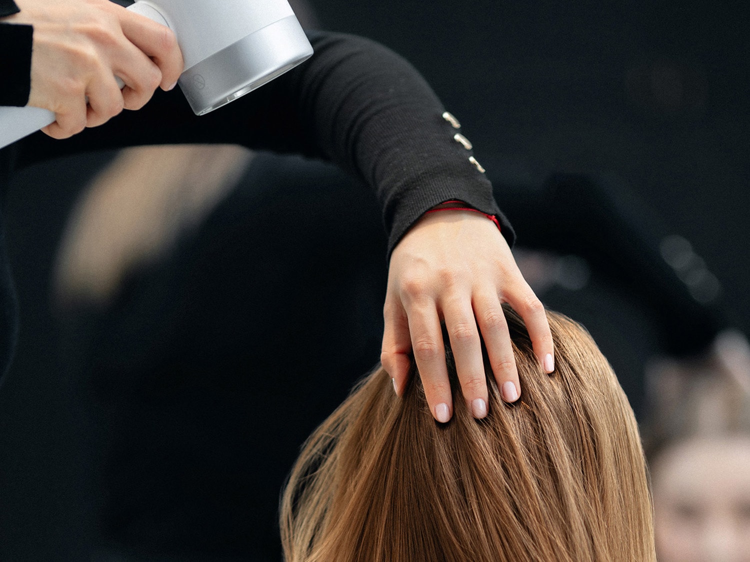 Fryzjer stylizuje włosy klientki za pomocą białej suszarki, delikatnie dotykając jej włosów.