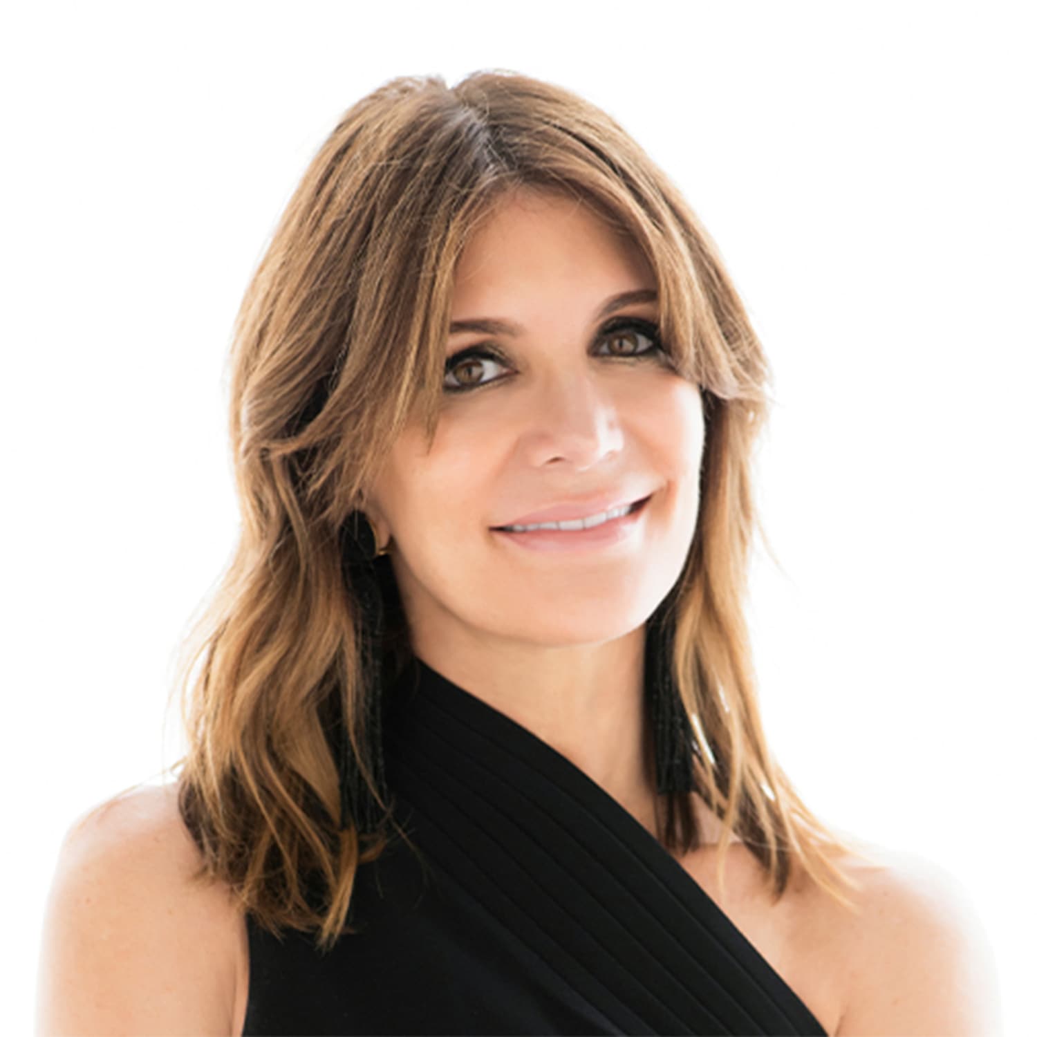 Porträt einer Frau mit gewelltem, braunem Haar, die ein ärmelloses, schwarzes Kleid trägt und Ohrringe mit Fransen.