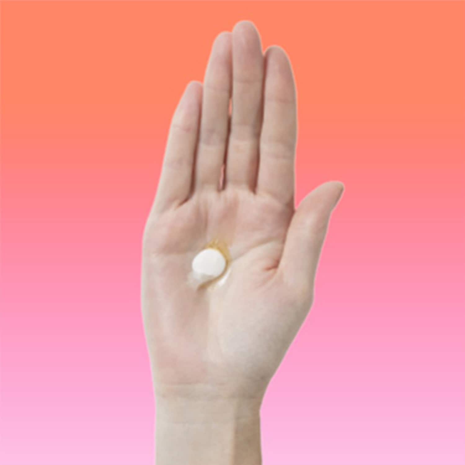 Auf einer geöffneten Handfläche liegt eine einzelne, runde, weiße Tablette, die sich vor einem Hintergrund in Pfirsich- und Rosatönen abhebt.