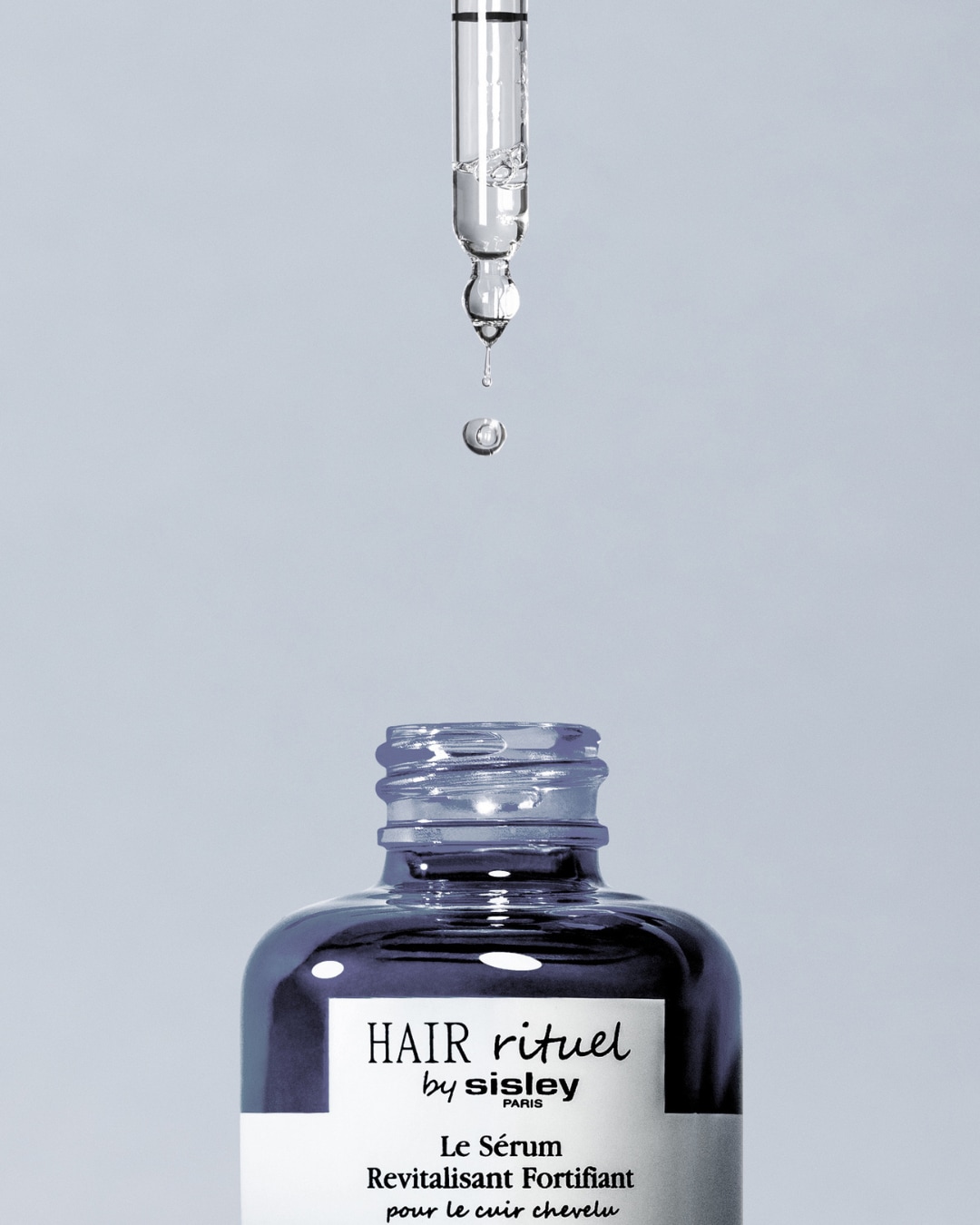 Découvrez le Sérum Revitalisant Fortifiant pour le cuir chevelu de Hair Rituel by Sisley, présenté dans un flacon élégant avec une pipette laissant tomber une goutte de sérum.