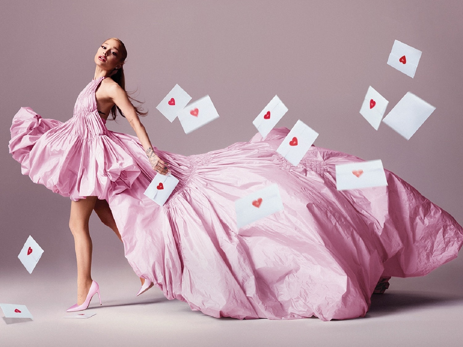 Eine Frau in einem bauschigen, rosa Kleid und passenden Absätzen posiert, während Briefe mit roten Herzaufklebern um sie herum schweben.