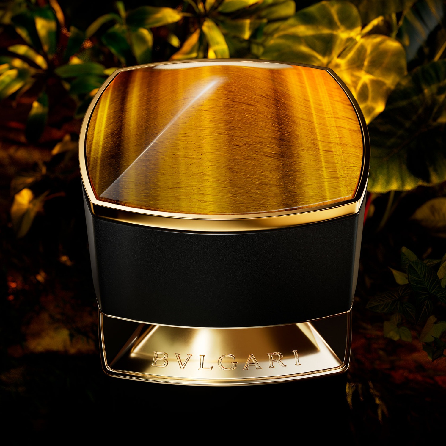 Nahaufnahme des Bvlgari-Parfums in einer schwarzen und goldenen Flasche mit einem Tigerauge-artigen Deckel vor einem Hintergrund aus üppigem Grün.