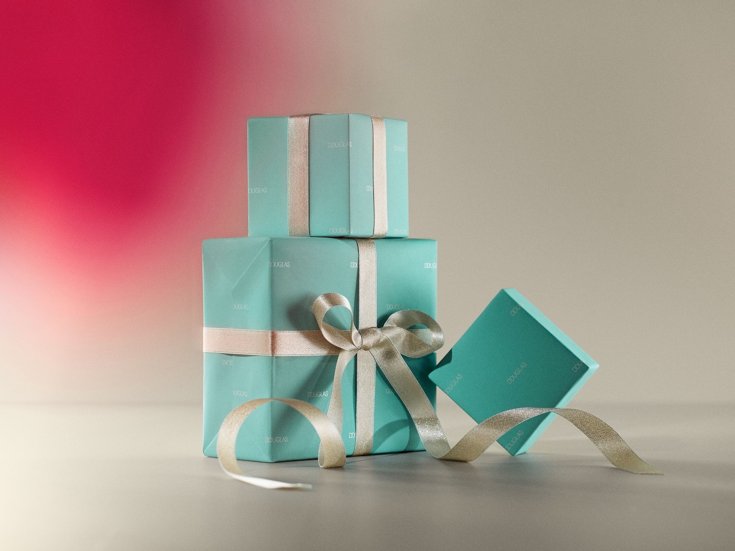 Tři dárkové krabičky Douglas v odstínech modré a tyrkysové jsou naskládané na sobě a ozdobené stříbrnými stuhami, které dodávají elegantní vzhled.