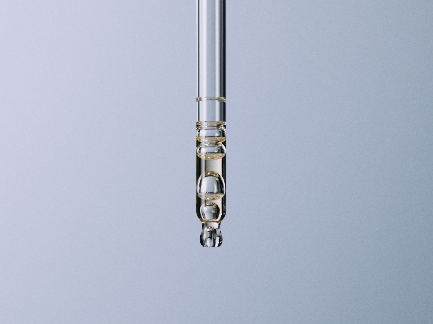 Close-up van een glazen pipet gevuld met een heldere, gouden vloeistof, klaar om druppelsgewijs te doseren voor huidverzorging.