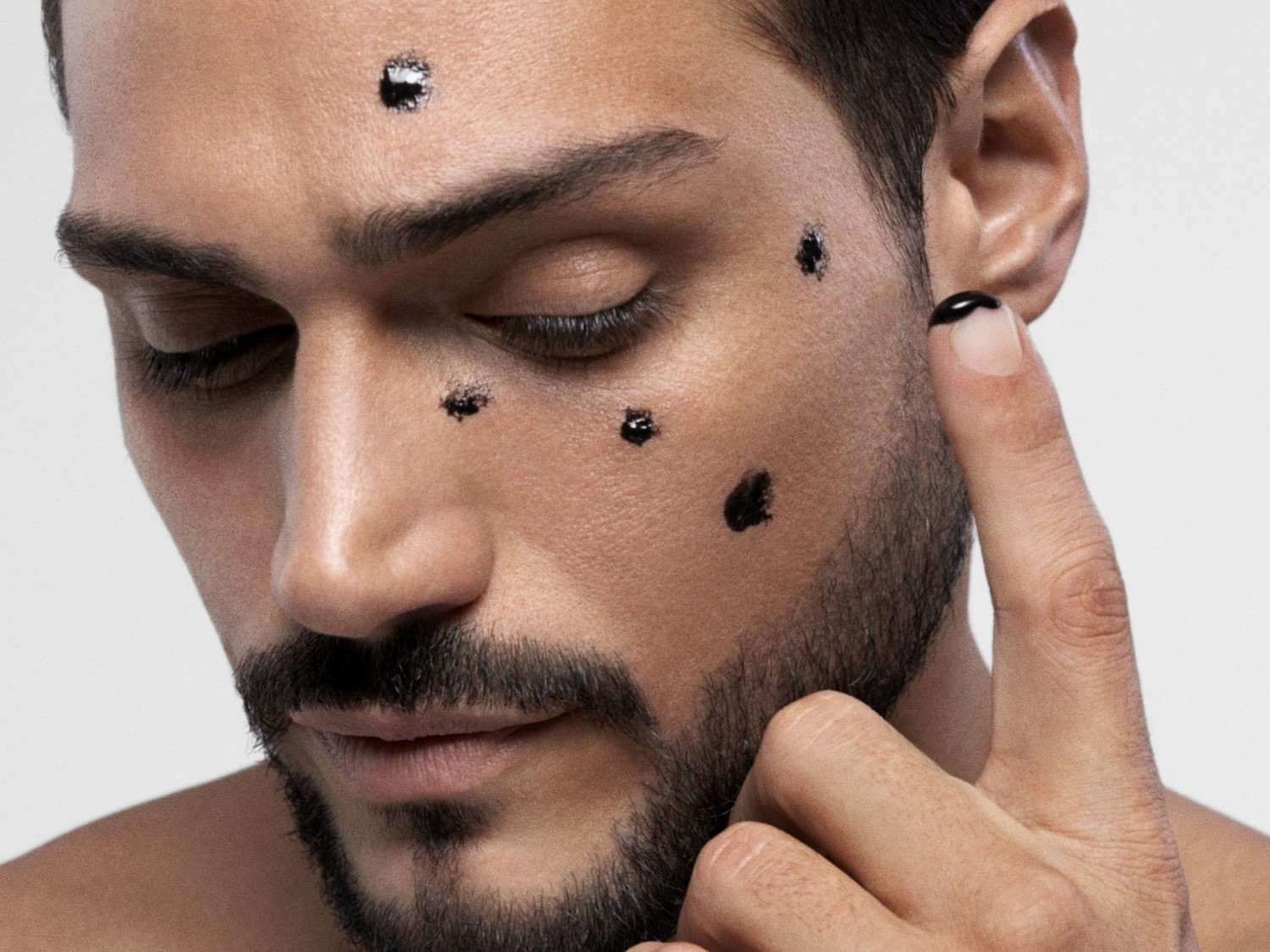 Gros plan sur un homme appliquant un masque noir sur son visage avec le doigt, pour une peau purifiée et éclatante.