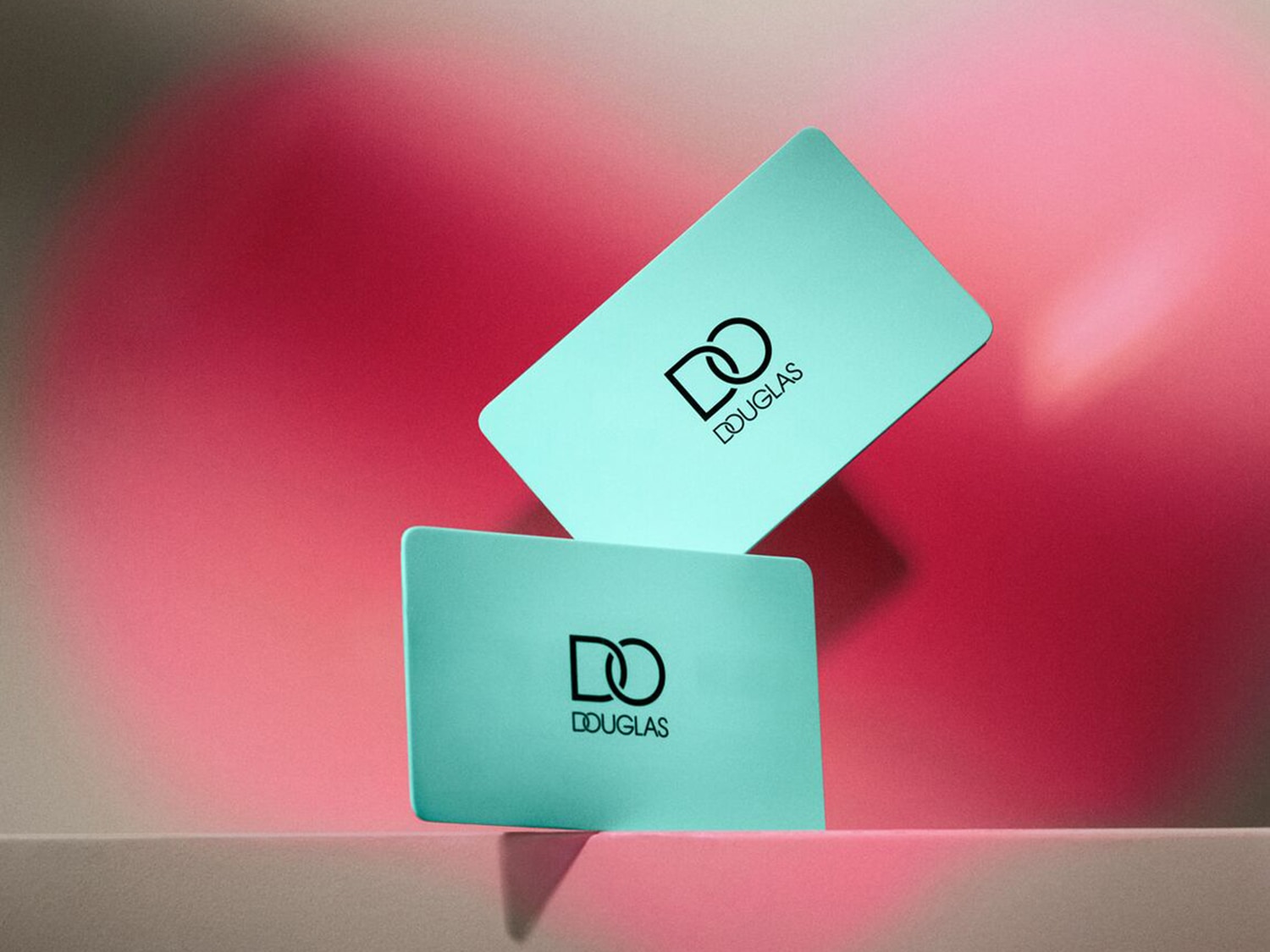 Dve svetlomodré darčekové karty Douglas s čiernym logom na ružovom pozadí.