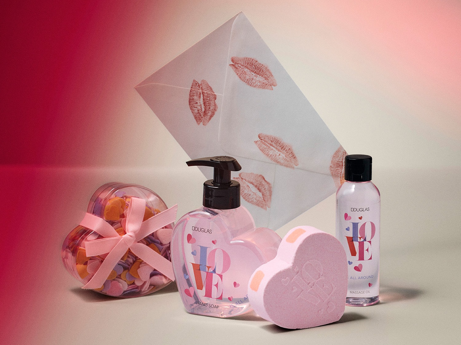Súprava produktov Douglas v tvare srdca s mydlom na ruky, masážnym olejom a srdiečkovou bombou do kúpeľa, doplnená o valentínsku obálku s odtlačkami bozkov a ozdobnú krabičku v tvare srdca.