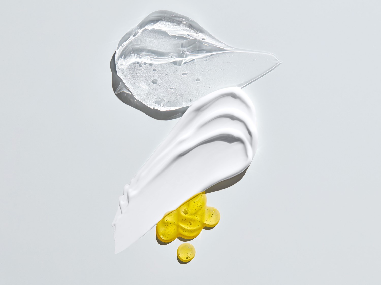 Drei Texturen sind zu sehen: ein durchsichtiges Gel, eine weiße Creme und ein goldenes Öl, die die Vielfalt der Schönheitsprodukte hervorheben.