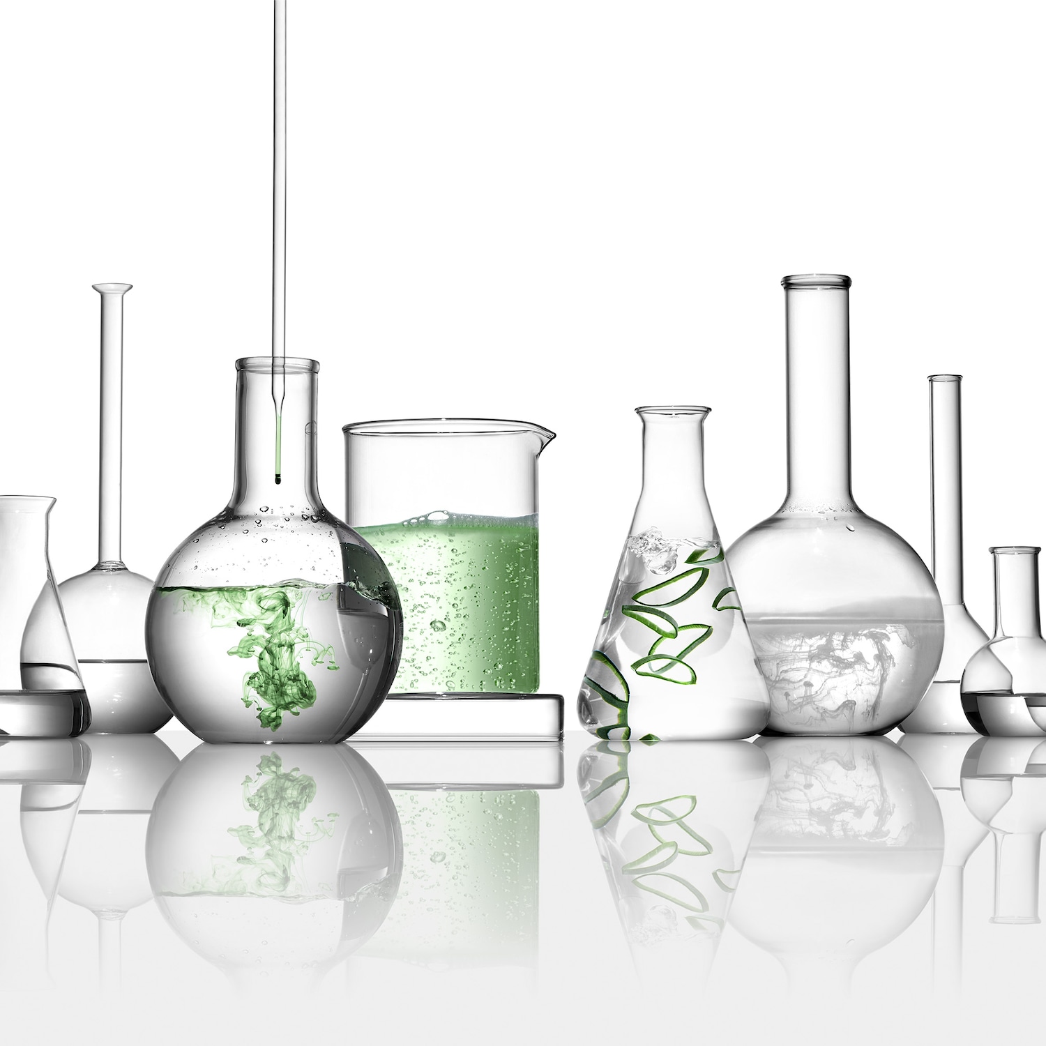Verschiedene Laborbehälter, einige mit grünen Flüssigkeiten und Aloe Vera, stehen auf einer reflektierenden Oberfläche.