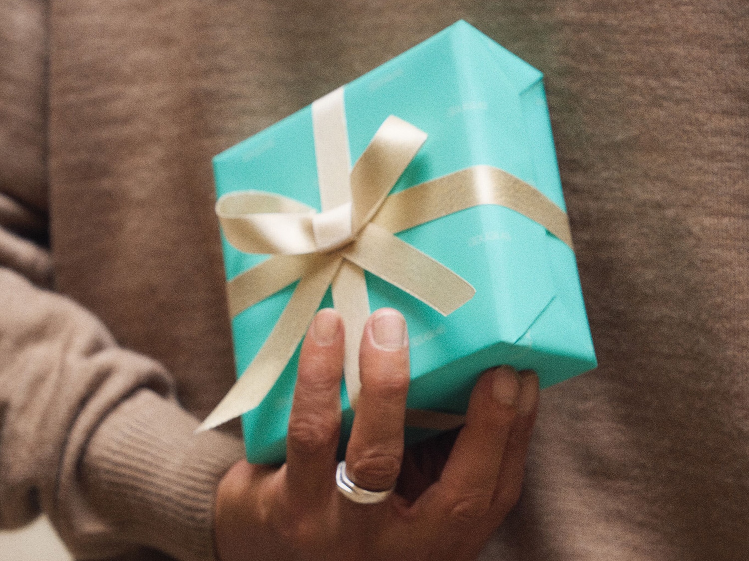 Detail muže držícího v ruce malý, světle modrý dárek s béžovou stuhou, ideální pro zvláštní příležitosti.