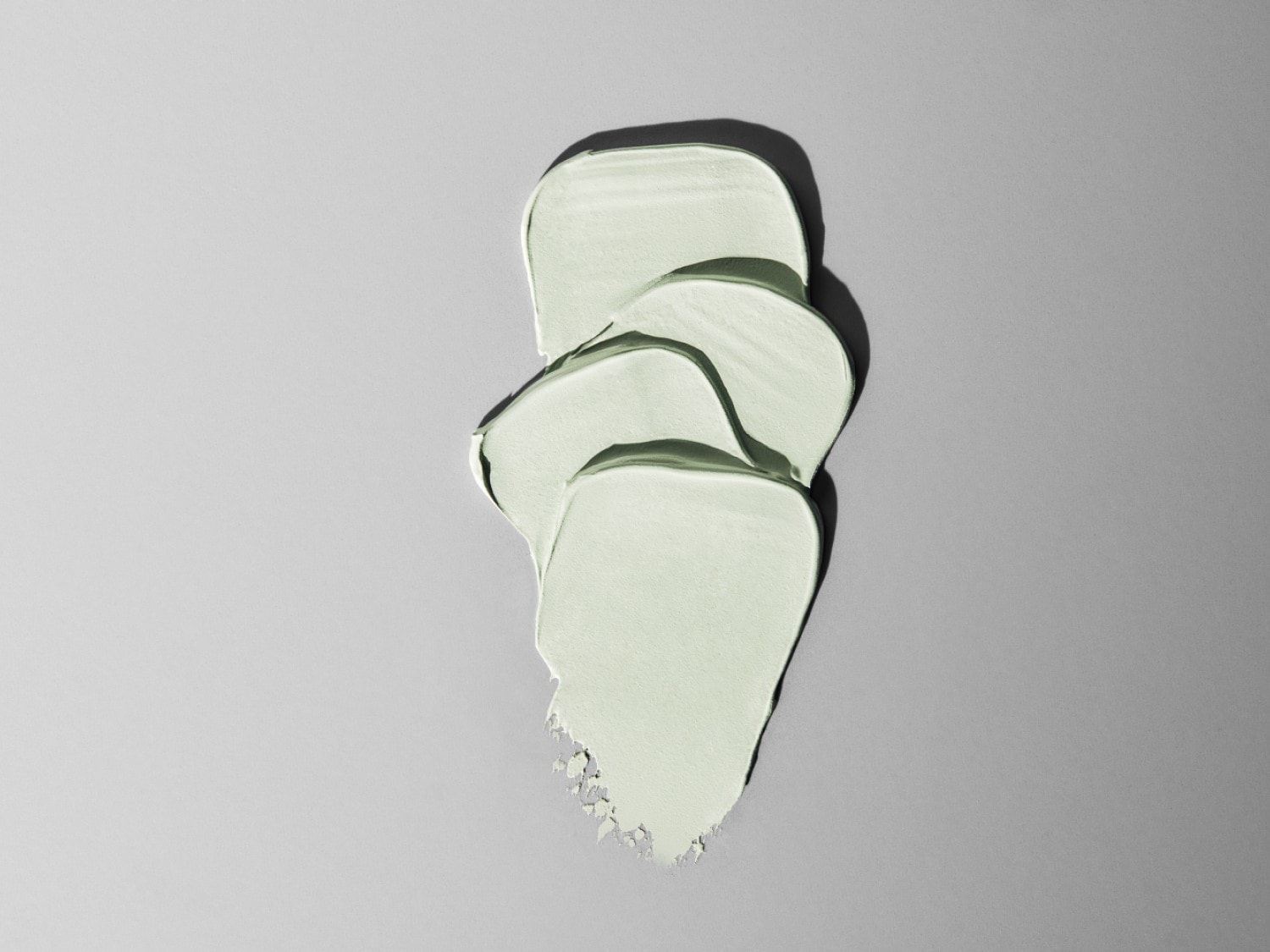 Textuur van een lichtgroen cosmetisch product, zoals een masker of crème, uitgesmeerd op een grijze achtergrond.